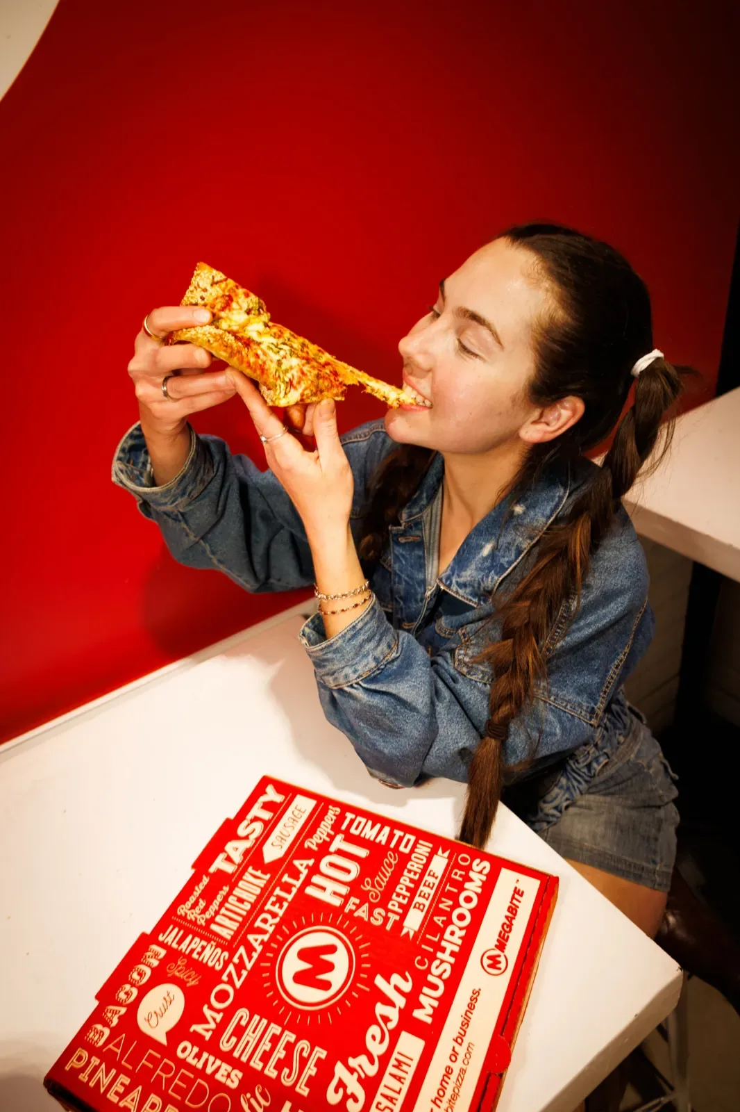 A guest taking a big bite of a slice against a red wall